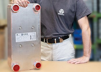 Auf einem Tisch steht ein Plattenwärmetauscher, dahinter steht ein Mitarbeiter in Hennlich Shirt